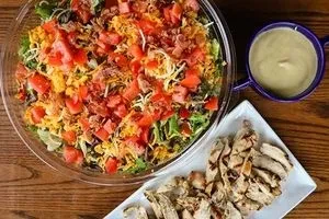 Overhead view of colorful salad, grilled chicken, and dressing.