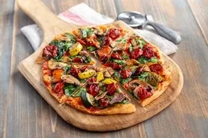 Freshly baked vegetable pizza with colorful toppings on a wooden peel.