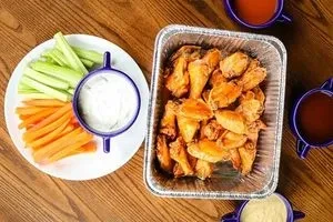 Golden-brown chicken wings, celery, carrots, and dips on a wooden table.