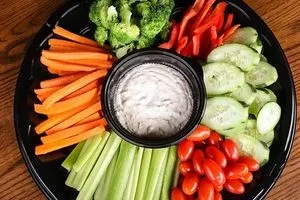 Circular black platter with assorted fresh cut vegetables and a central dip.