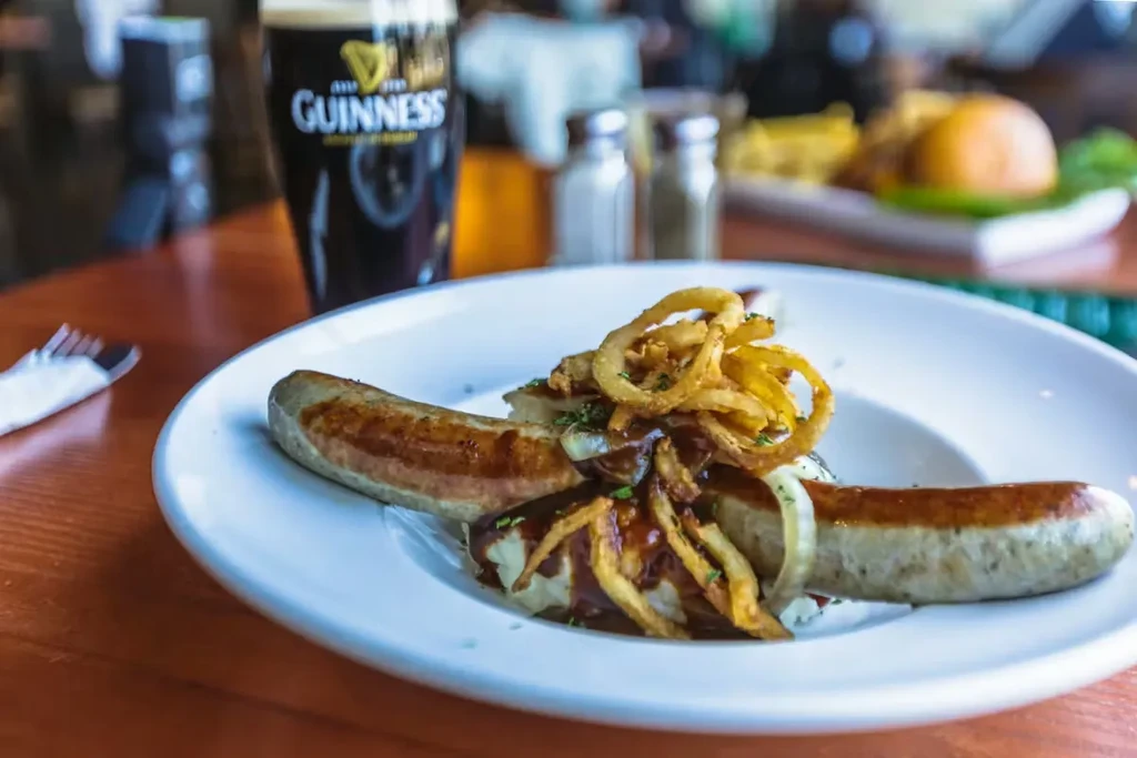 Grilled sausages, onion rings, mashed potatoes, and Guinness on a wooden table.