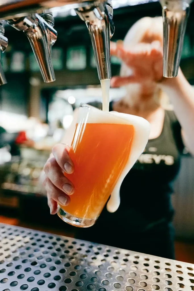Hand holds glass as beer pours from tap, overflowing with foam.