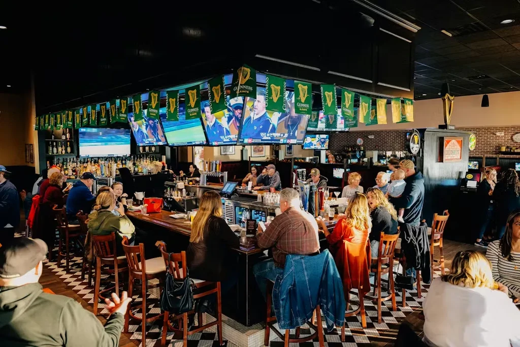 Busy Irish sports bar interior with patrons, TVs, and checkered floor.