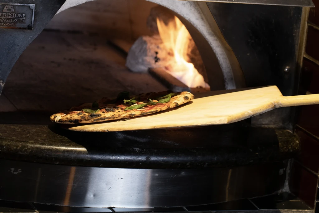 Wood-fired pizza with basil on peel entering oven.