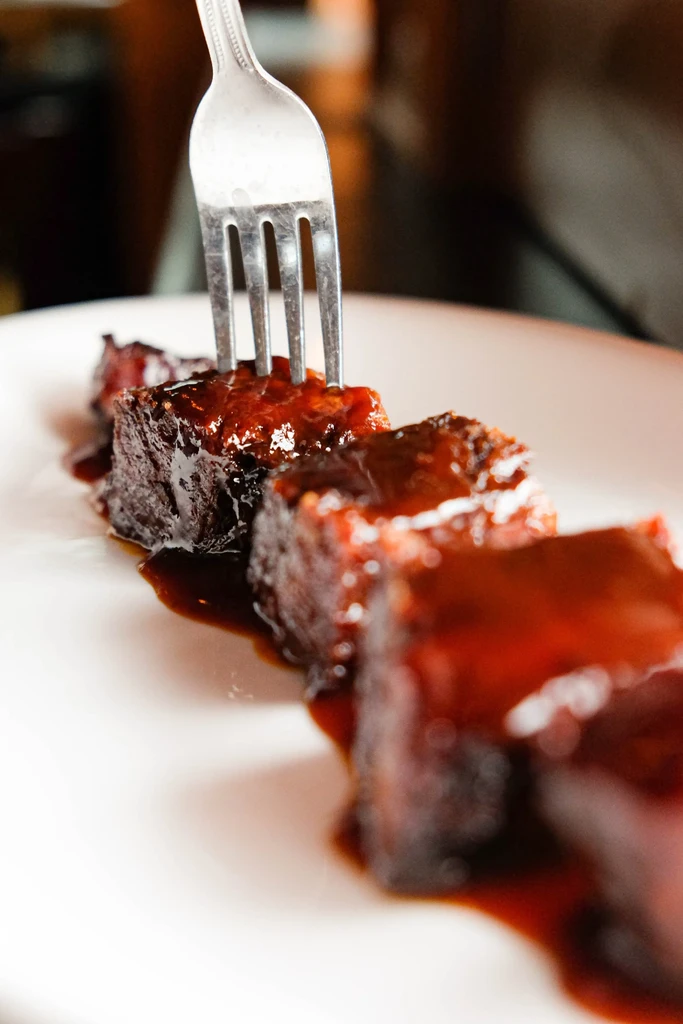 Fork piercing glistening glazed short ribs on a white plate.