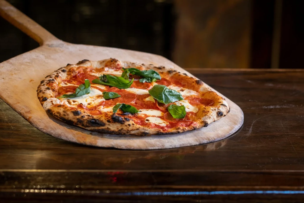 Neapolitan pizza with tomato, mozzarella, and basil on a wooden peel.