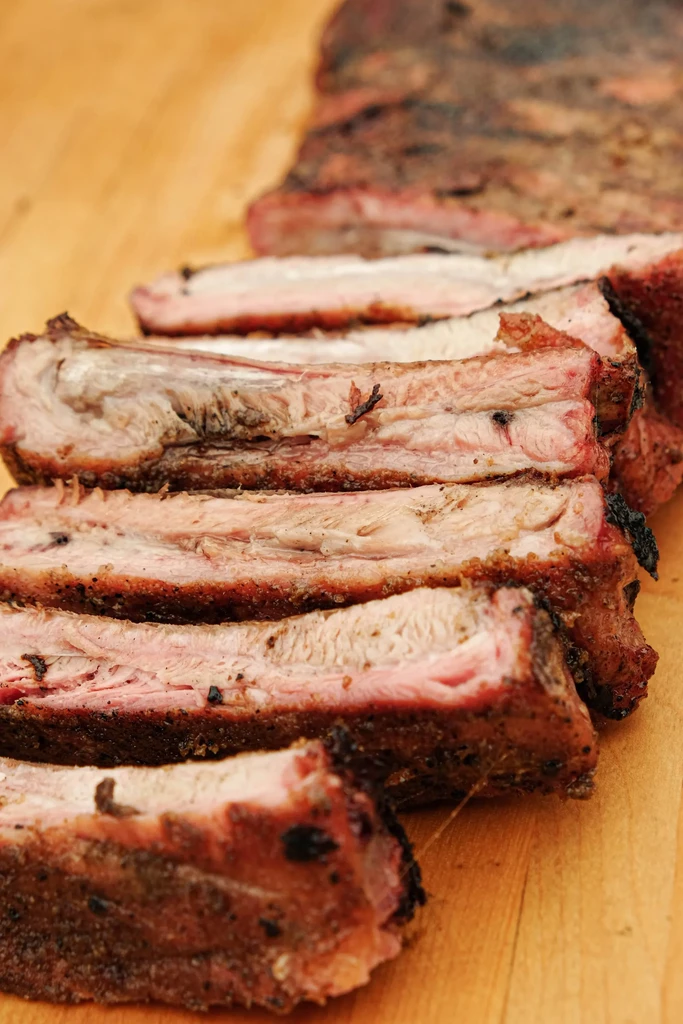 Sliced cooked pork ribs with pink meat and dark crust on wood.