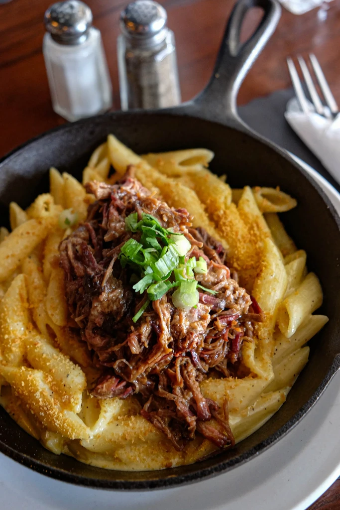Penne mac and cheese topped with shredded meat in a cast-iron skillet.