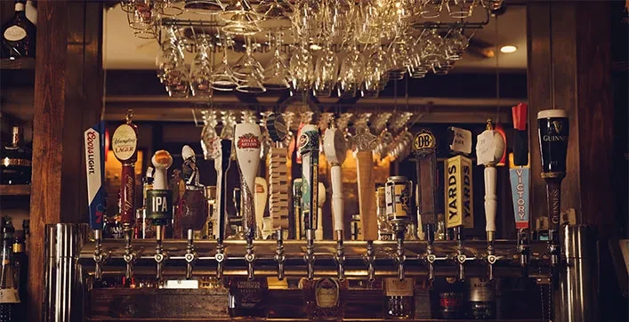 Numerous beer taps, hanging glasses, and a reflective bar background.