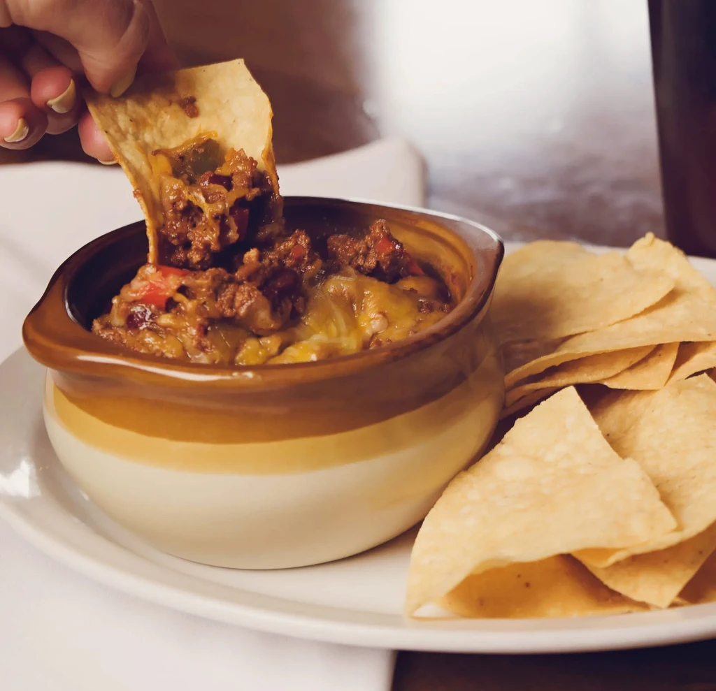 A hand dips a tortilla chip into a bowl of chili cheese dip.