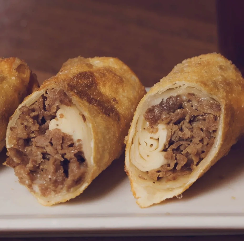 Crispy fried rolls, two cut open, revealing steak and cheese filling.