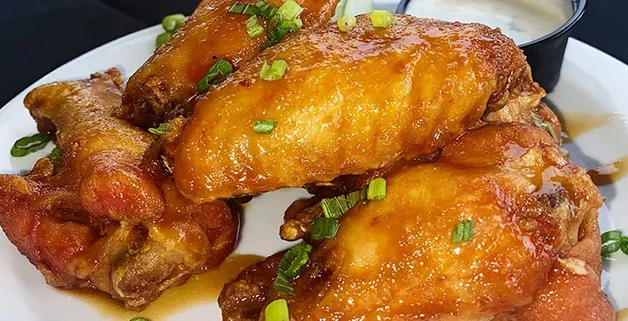 Golden-brown glazed chicken wings with green onions and dipping sauce.