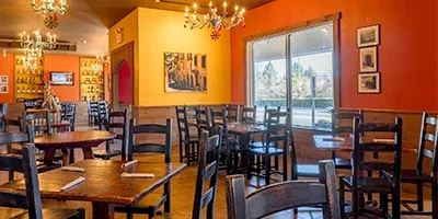 Empty restaurant dining room with warm walls, dark wood, and chandeliers.