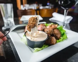 Fork lifting sauced meat from a plate of lettuce in a restaurant.