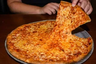 Hands lift a golden cheese pizza slice, creating a long cheese pull.