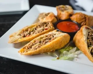 Meat-filled golden-brown rolls with red dipping sauce on a white plate.
