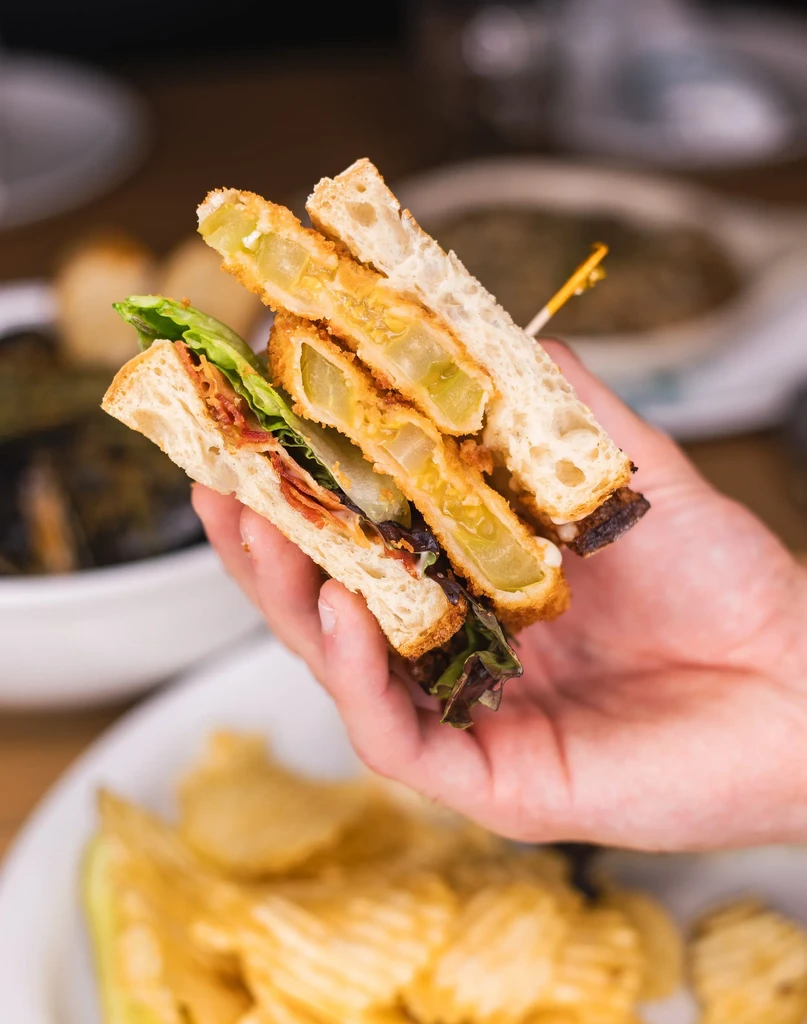 Hand holding a sandwich with fried green tomatoes, bacon, and lettuce.