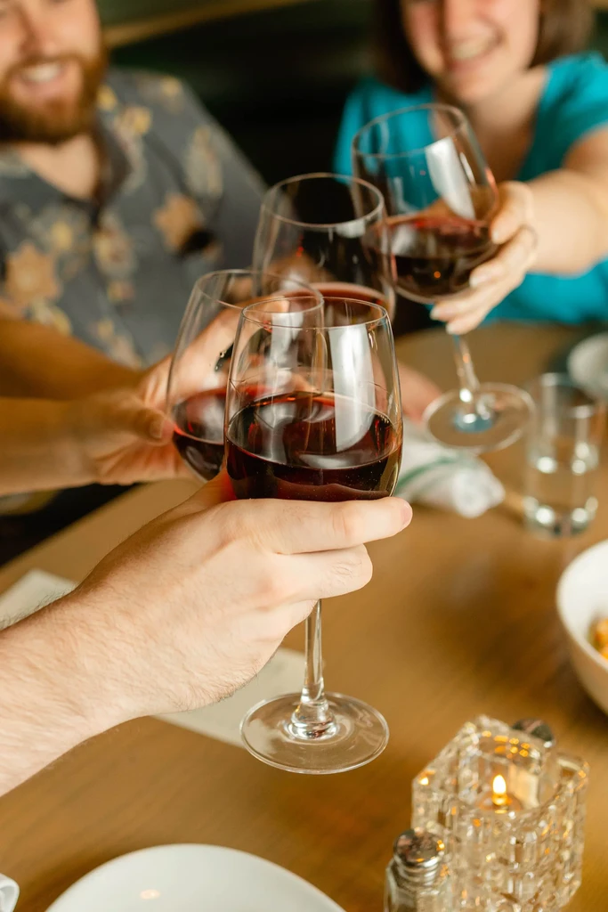 Hands clinking red wine glasses in a restaurant toast.