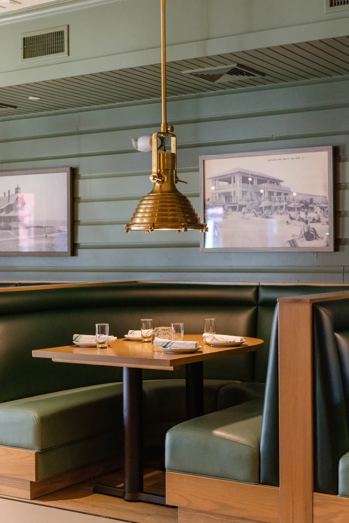 Empty dark green leather booth, wooden table, and brass light fixture.