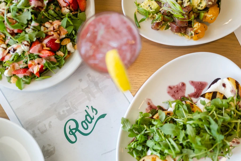 Overhead shot of two salads, a poke bowl, and a pink drink.