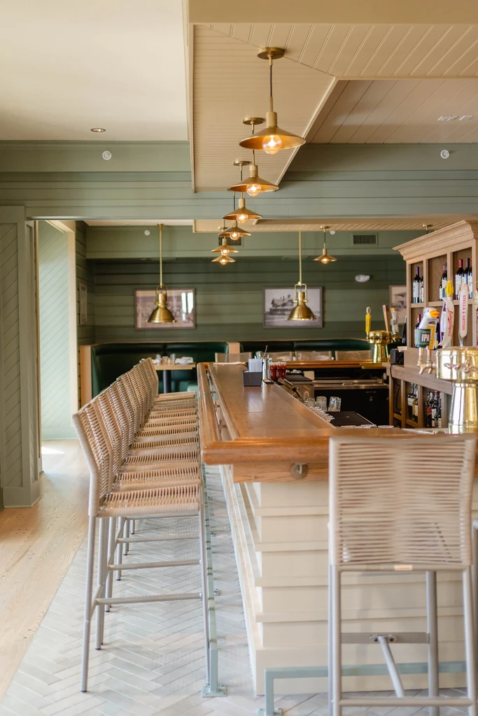 Empty restaurant interior with polished wooden bar, modern stools, olive-green walls.