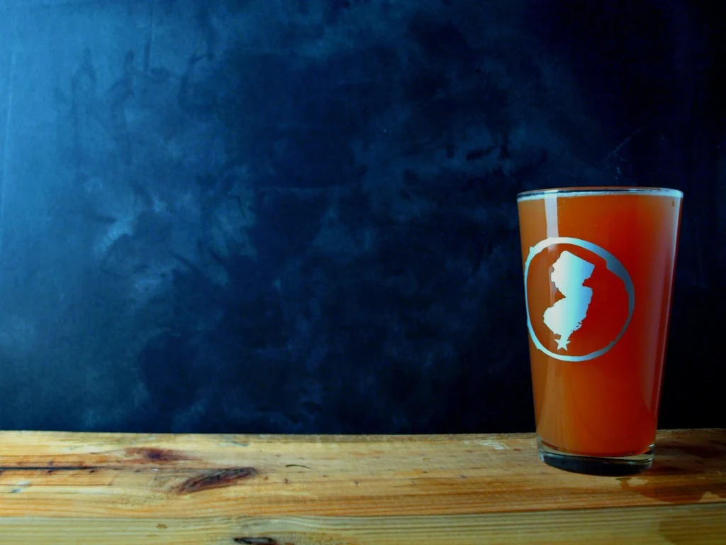 Glass with orange drink, etched New Jersey outline, on rustic wood.