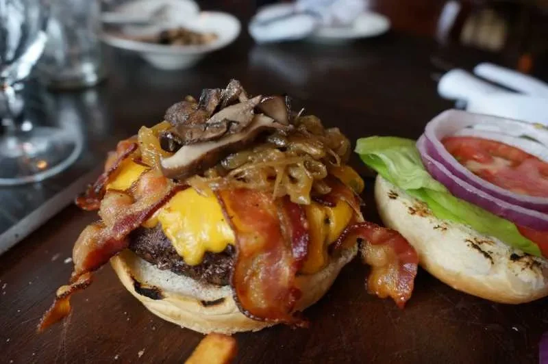 Open-faced gourmet beef burger with bacon, cheese, mushrooms, and fresh vegetables.