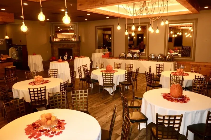 Warmly lit autumn event space with pumpkin centerpieces and buffet.