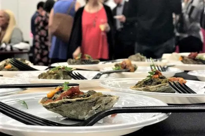 Close-up: Individual oyster appetizers with forks at a social gathering.