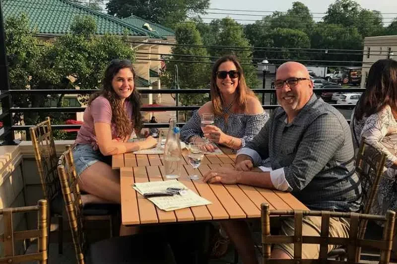 Three smiling people at an outdoor table with city views.