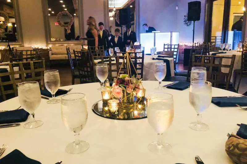 Elegant indoor event space with set tables, terrarium centerpieces, and DJ.