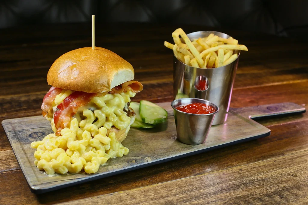 Burger topped with mac and cheese, bacon, fries, and pickles.