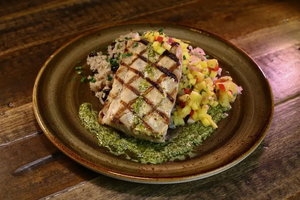 Grilled fish with char marks, rice, black beans, mango salsa, green sauce.