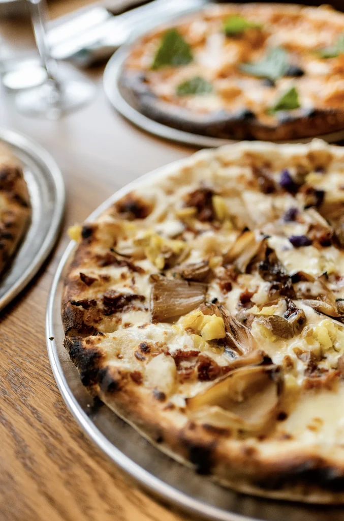 A white-base pizza and a red-sauce pizza on a wooden table.
