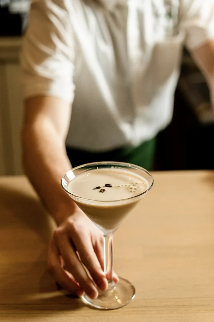Creamy martini with coffee beans and bubbles, held by a server.