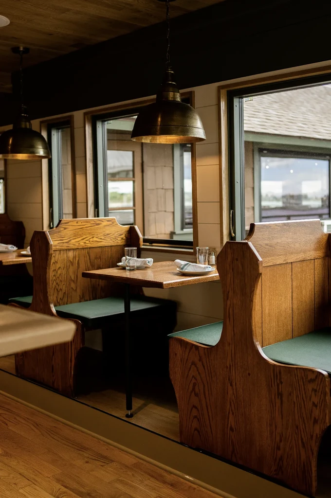 Wooden restaurant booths with green cushions, brass lights, window view.
