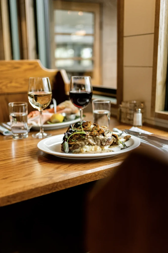 Restaurant table with a meat dish, creamy sauce, mushrooms, and wine.