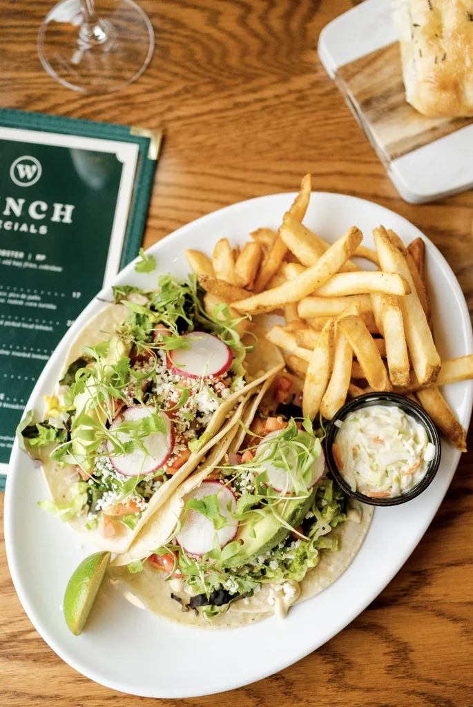 Two garnished tacos, french fries, and coleslaw on a white plate.