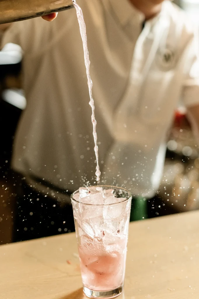 Bartender pouring pink drink into ice-filled glass, creating a splash.