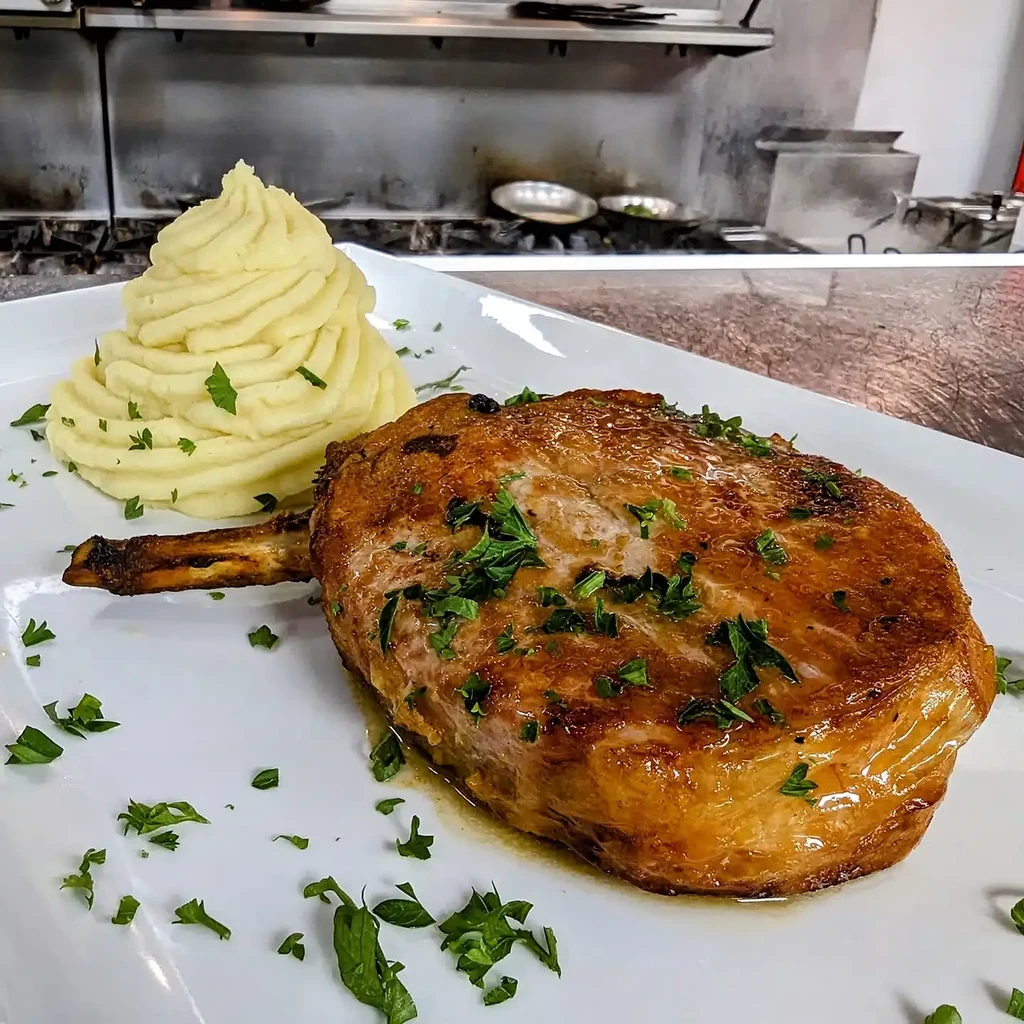 Golden-brown bone-in meat, mashed potatoes, and parsley on a plate.