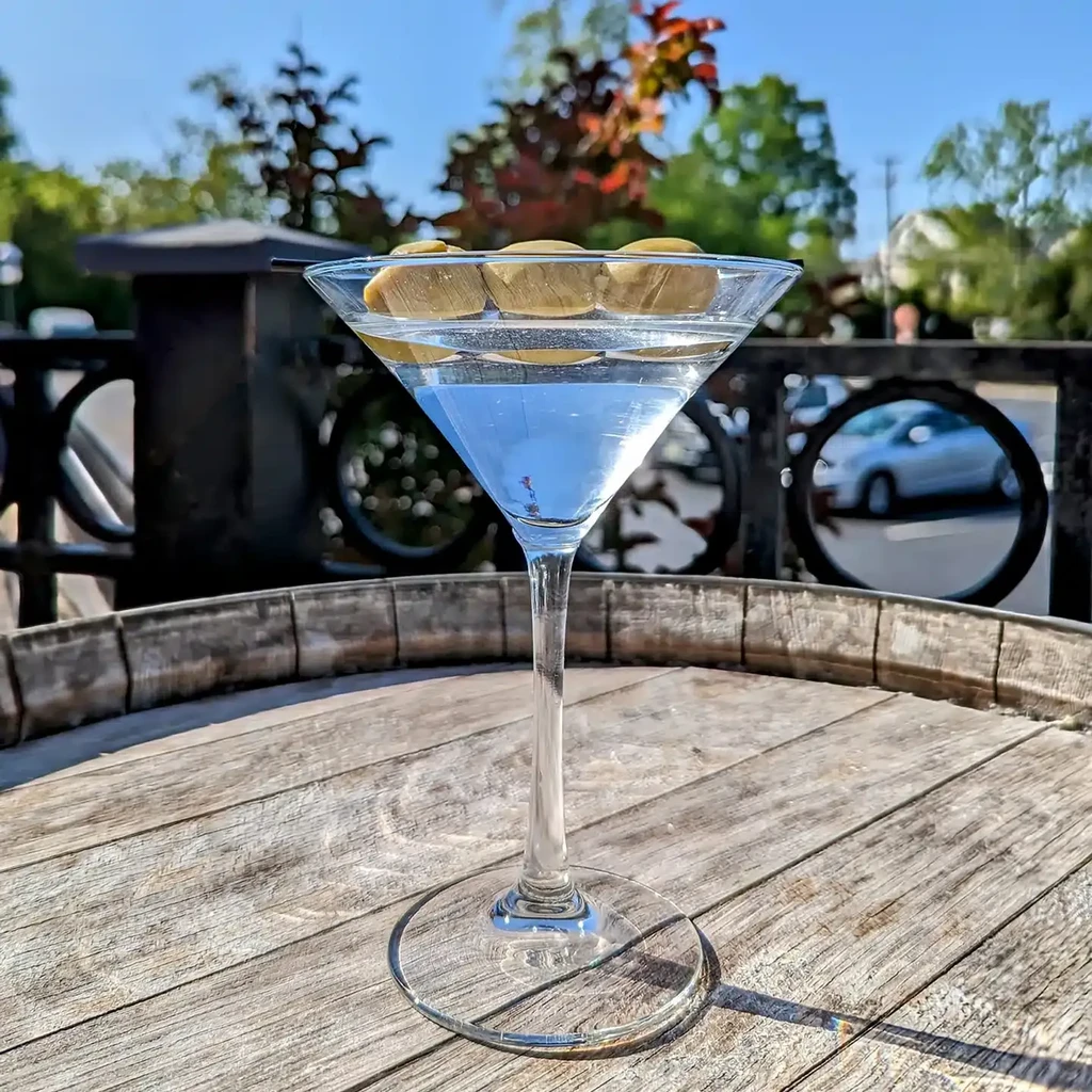 Light blue martini with four olives on a rustic wooden barrel table.