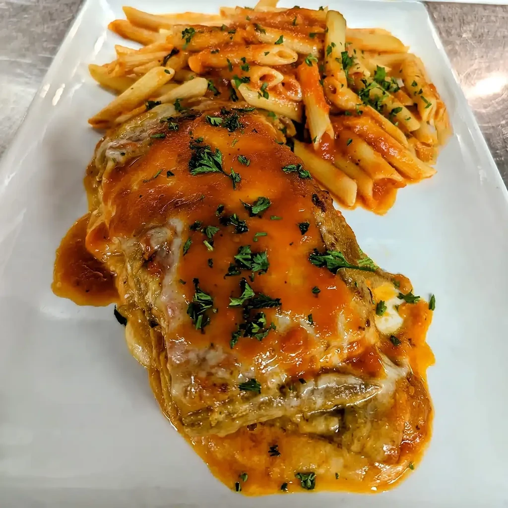 Prepared meal with sauced protein, melted cheese, penne pasta, and herbs.
