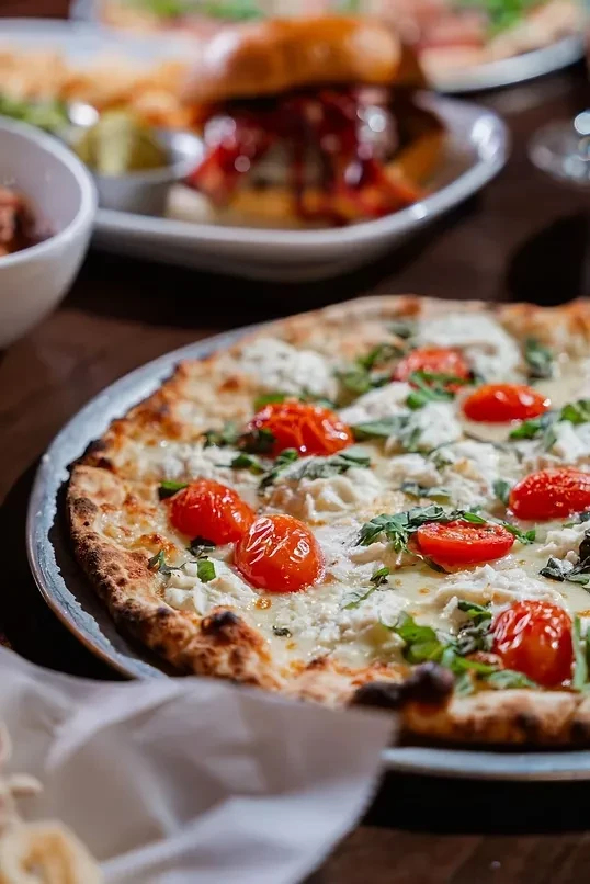 Close-up pizza with melted cheese, roasted tomatoes, and fresh basil.