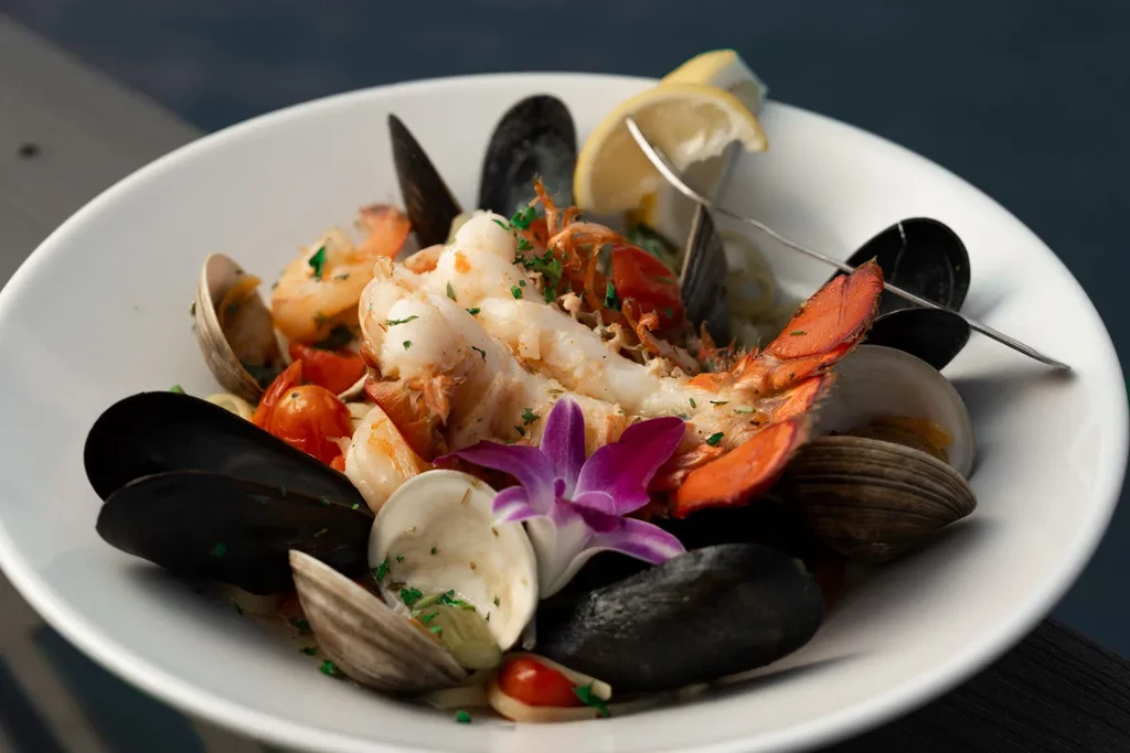 Cooked lobster tail, mussels, shrimp, and clams in a white bowl.