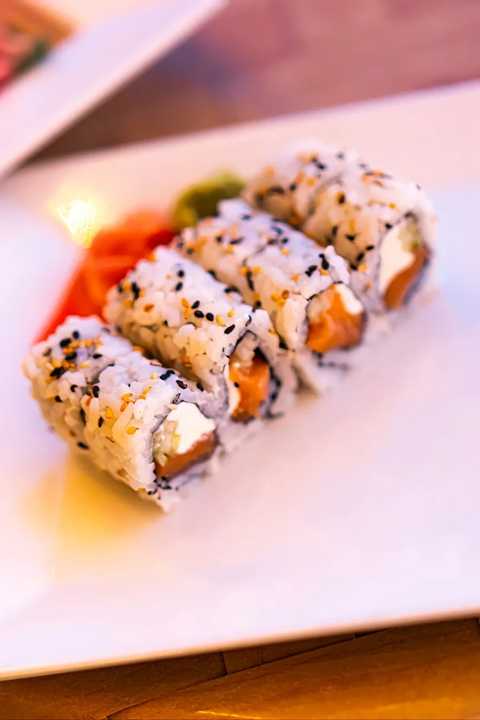 Four sushi rolls with salmon, cream cheese, sesame, ginger, and wasabi.