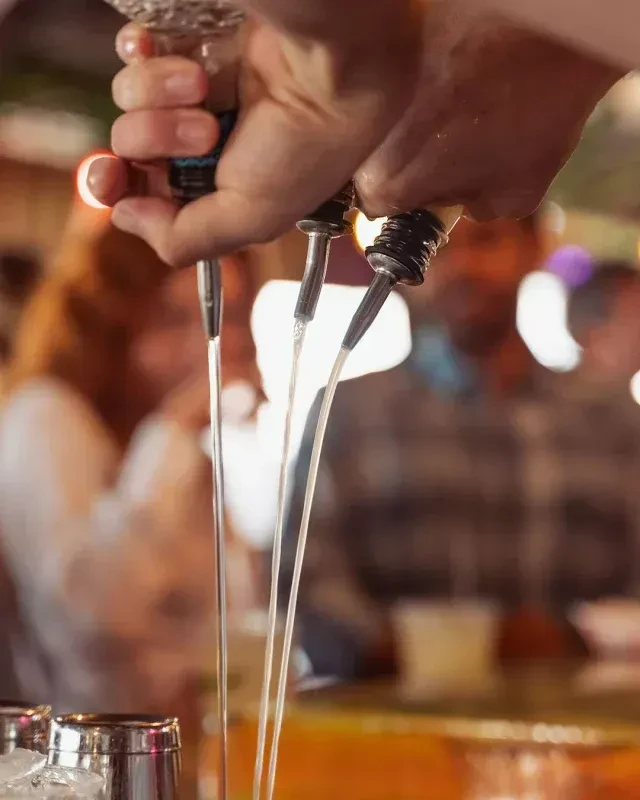 Close-up of hands pouring three liquids into a shaker at a bar.