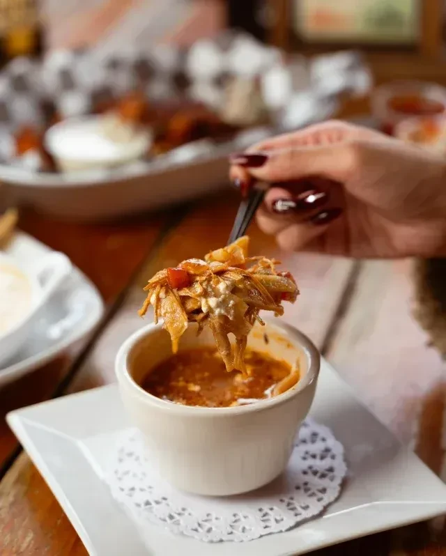 Hand with red nails spoons creamy, garnished food from a cup.