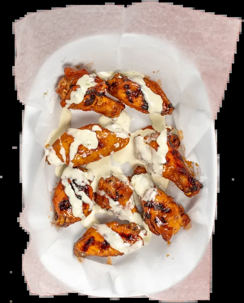 Eight golden-brown crispy chicken wings with creamy sauce in white dish.