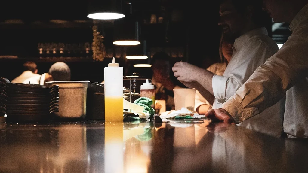 Reflective counter with squeeze bottles, plates, and blurred kitchen staff working.