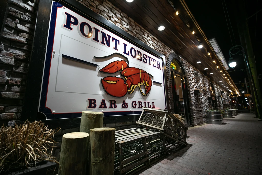 Point Lobster Bar & Grill's bright sign and rustic lobster traps at night.